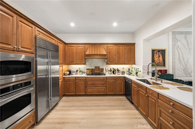 kitchen with built in appliances, tasteful backsplash, sink, light wood-type flooring, and custom range hood