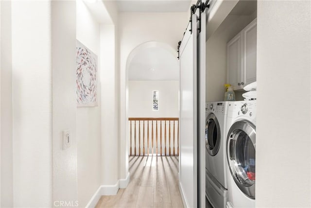 clothes washing area featuring a barn door, light wood-type flooring, independent washer and dryer, and cabinets