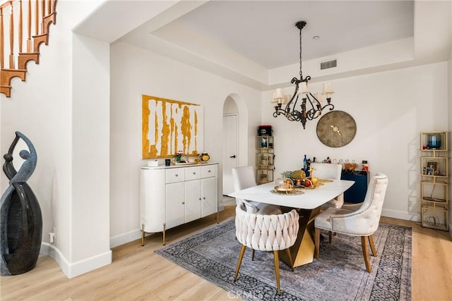 dining space with a chandelier, light hardwood / wood-style floors, and a raised ceiling