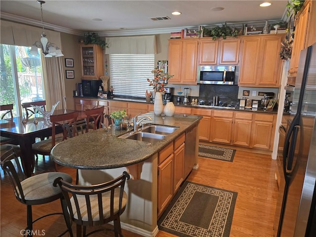 kitchen featuring sink, ornamental molding, pendant lighting, stainless steel appliances, and a kitchen island with sink