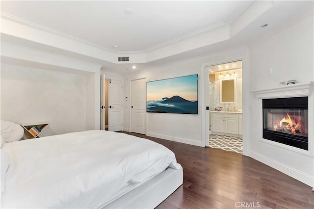 bedroom with connected bathroom, a tray ceiling, dark hardwood / wood-style flooring, and ornamental molding