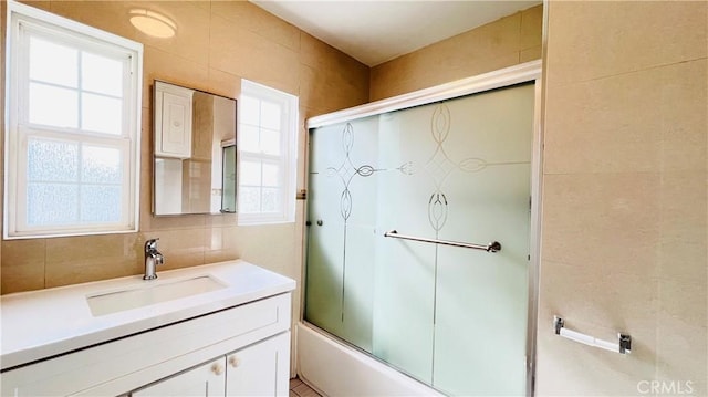 bathroom featuring combined bath / shower with glass door, vanity, tile walls, and tasteful backsplash