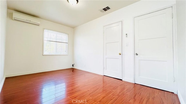 unfurnished bedroom featuring wood-type flooring and a wall mounted air conditioner