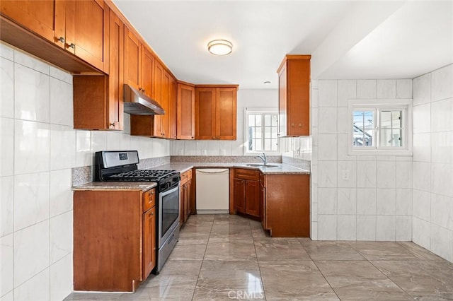 kitchen featuring white dishwasher, sink, stainless steel range with gas stovetop, and tile walls