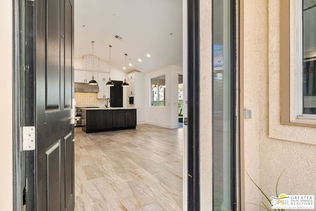 kitchen with vaulted ceiling, a kitchen island, pendant lighting, white cabinets, and backsplash