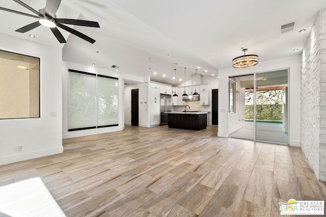 unfurnished living room featuring ceiling fan with notable chandelier and vaulted ceiling