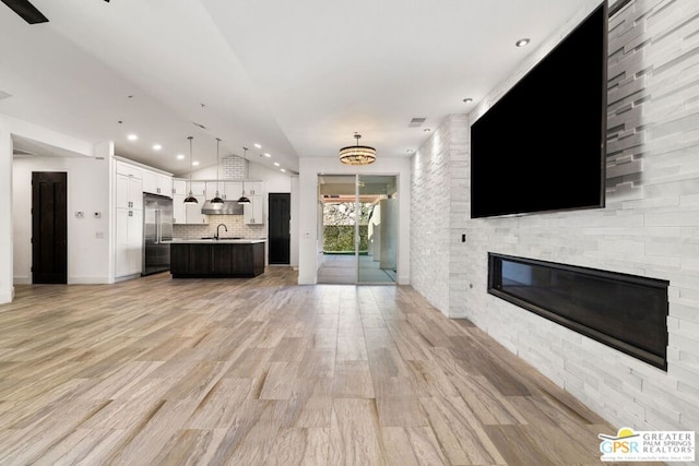 unfurnished living room featuring sink, an inviting chandelier, vaulted ceiling, light wood-type flooring, and a fireplace