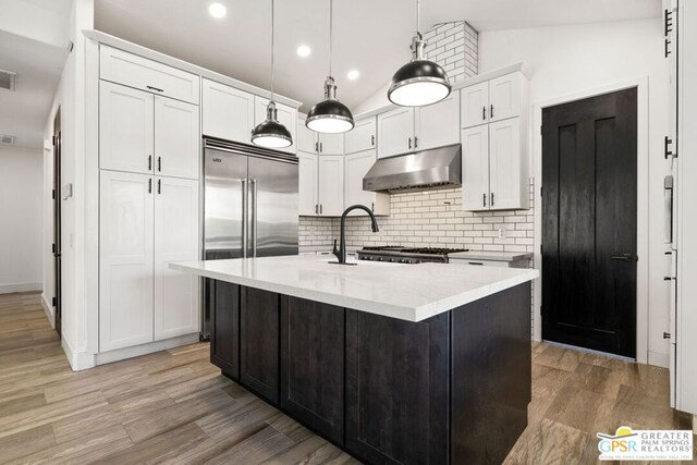 kitchen with pendant lighting, backsplash, light stone countertops, an island with sink, and white cabinets