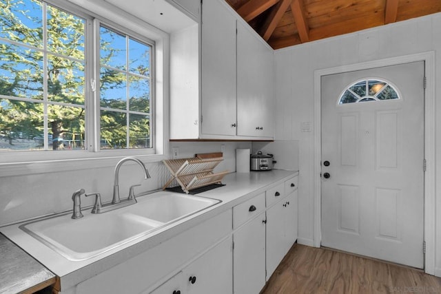 kitchen with lofted ceiling with beams, sink, white cabinets, and light hardwood / wood-style flooring