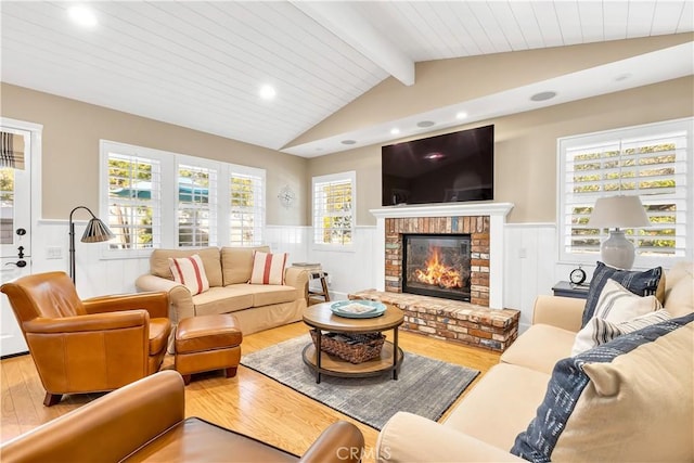 living room with a brick fireplace, plenty of natural light, wood-type flooring, and lofted ceiling with beams