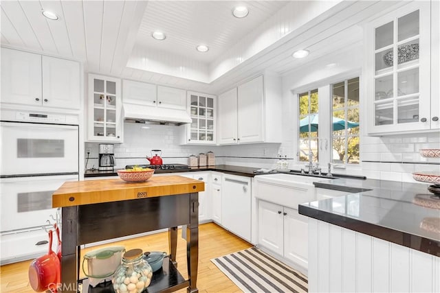 kitchen with white appliances, white cabinets, decorative backsplash, a raised ceiling, and light wood-type flooring