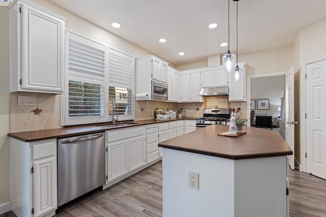 kitchen featuring appliances with stainless steel finishes, a center island, decorative light fixtures, white cabinetry, and tasteful backsplash