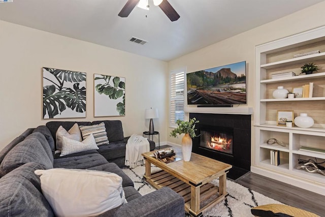 living room featuring ceiling fan, dark wood-type flooring, a tile fireplace, and built in features