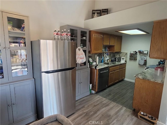 kitchen with dishwasher, stone counters, sink, dark wood-type flooring, and stainless steel fridge