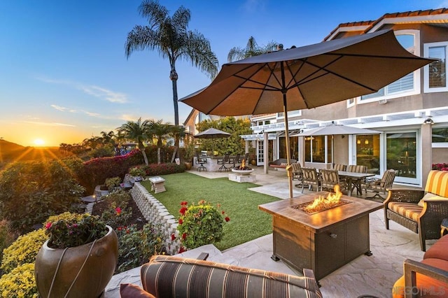 patio terrace at dusk featuring a yard, a pergola, and an outdoor living space with a fire pit