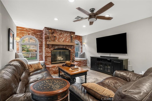 living room with ceiling fan, a brick fireplace, brick wall, and light hardwood / wood-style flooring