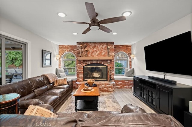 living room with ceiling fan, brick wall, a brick fireplace, and light wood-type flooring