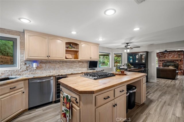 kitchen featuring wooden counters, a kitchen island, appliances with stainless steel finishes, light brown cabinetry, and beverage cooler