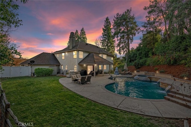 pool at dusk featuring a patio area, an in ground hot tub, a lawn, and pool water feature