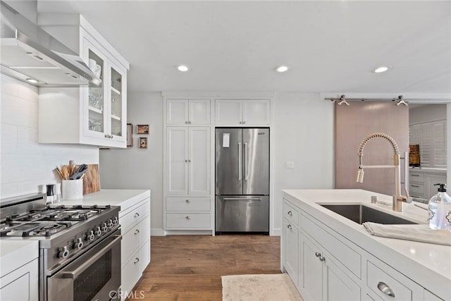 kitchen featuring appliances with stainless steel finishes, sink, white cabinets, dark hardwood / wood-style flooring, and wall chimney range hood