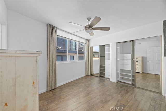 unfurnished bedroom featuring hardwood / wood-style floors, two closets, and ceiling fan