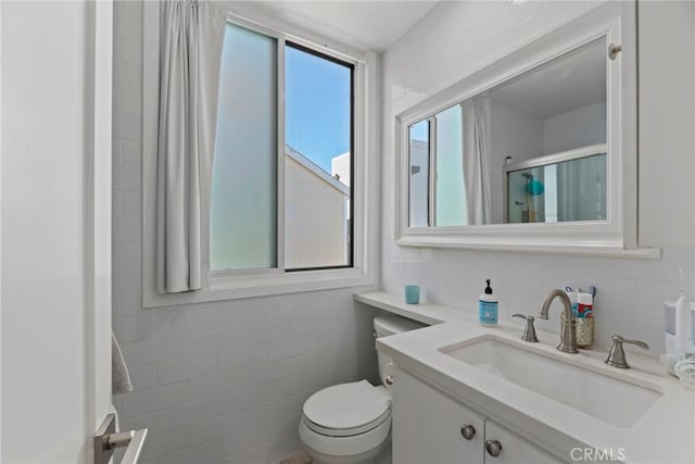 bathroom with tile walls, vanity, a shower with door, and toilet