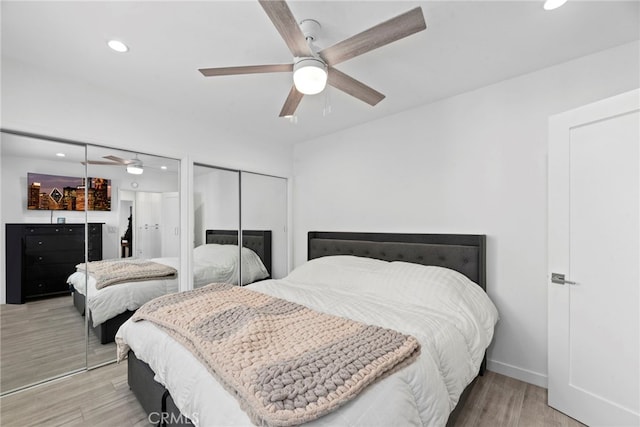 bedroom featuring multiple closets, light hardwood / wood-style flooring, and ceiling fan