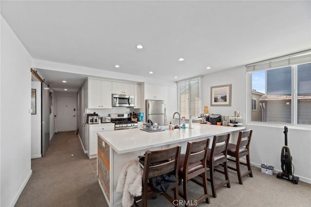 kitchen with white cabinetry, tasteful backsplash, light carpet, a kitchen breakfast bar, and stainless steel appliances