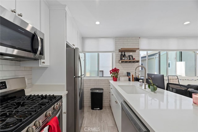 kitchen with sink, white cabinetry, backsplash, stainless steel appliances, and light wood-type flooring