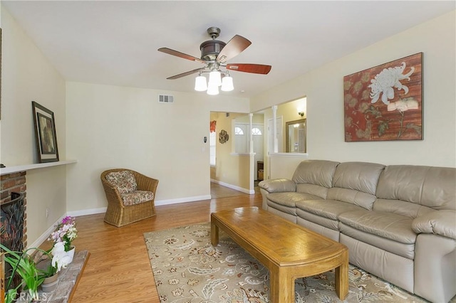 living room featuring ceiling fan, light wood-type flooring, and a brick fireplace