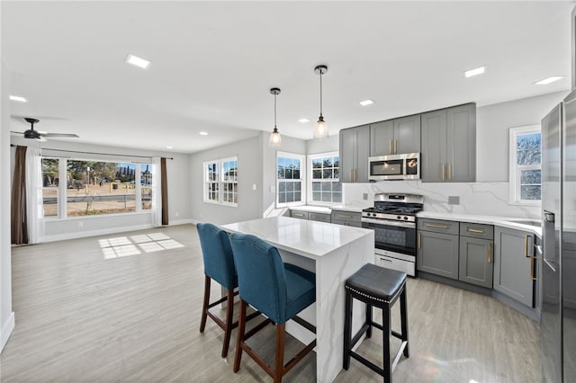 kitchen with stainless steel appliances, gray cabinetry, hanging light fixtures, light hardwood / wood-style flooring, and a breakfast bar