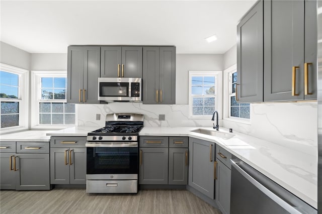 kitchen with tasteful backsplash, sink, light hardwood / wood-style flooring, appliances with stainless steel finishes, and gray cabinetry