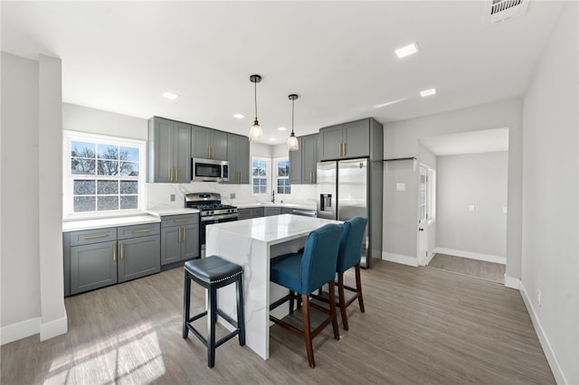 kitchen with light hardwood / wood-style floors, a breakfast bar area, appliances with stainless steel finishes, hanging light fixtures, and a kitchen island