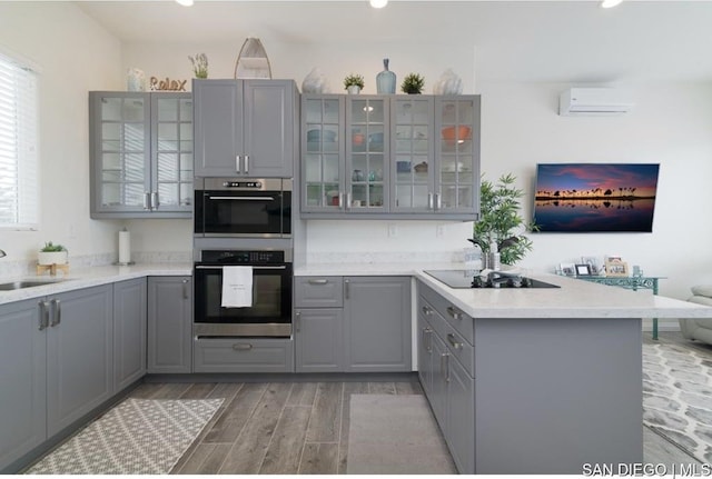 kitchen with gray cabinetry, black electric cooktop, sink, a wall unit AC, and double oven