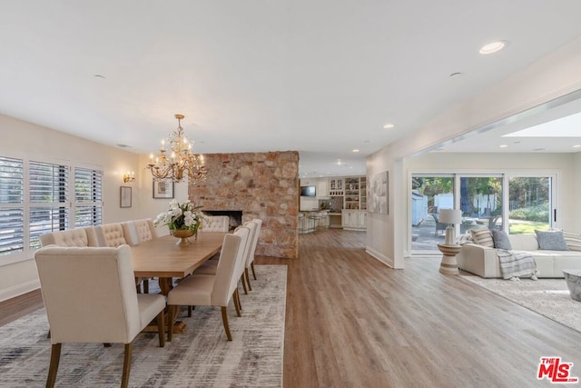 dining room with a stone fireplace, light hardwood / wood-style floors, and a notable chandelier