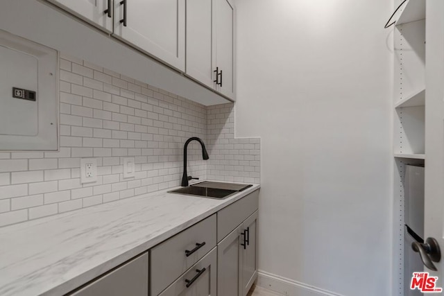 kitchen featuring sink, electric panel, light stone counters, tasteful backsplash, and white cabinets