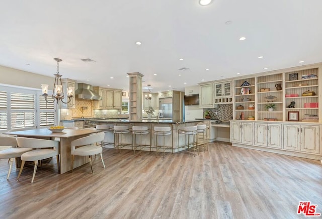 kitchen with pendant lighting, wall chimney exhaust hood, an inviting chandelier, and cream cabinetry