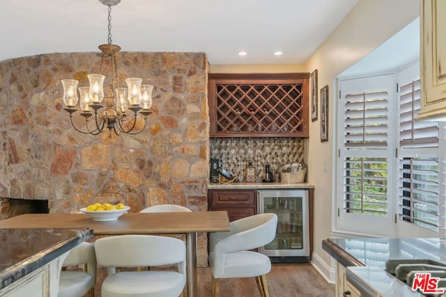 dining room featuring wine cooler, light wood-type flooring, an inviting chandelier, and bar area