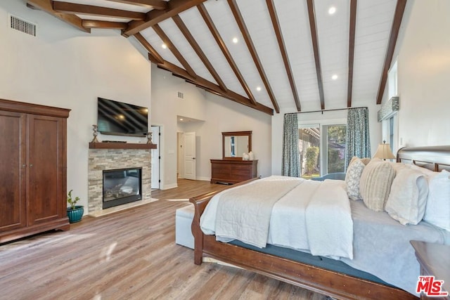 bedroom with a fireplace, high vaulted ceiling, beam ceiling, and light wood-type flooring