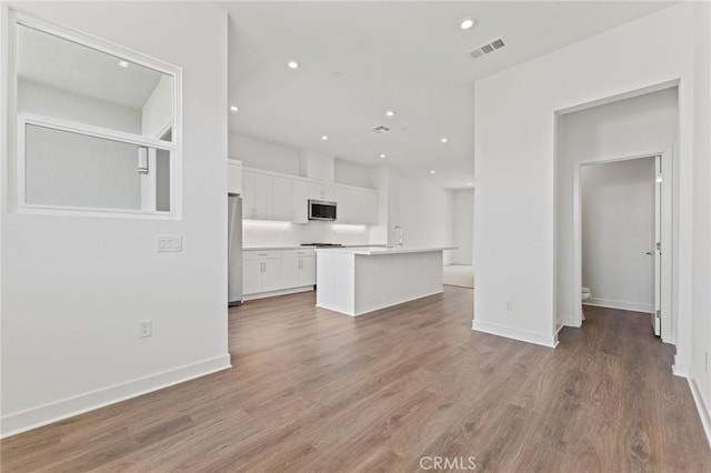 kitchen featuring hardwood / wood-style floors, white cabinets, stainless steel appliances, and a kitchen island with sink