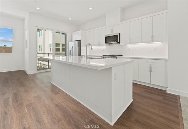 kitchen with sink, white cabinets, stainless steel appliances, and an island with sink