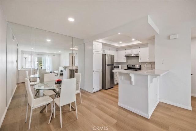 kitchen featuring light hardwood / wood-style flooring, a breakfast bar, appliances with stainless steel finishes, white cabinetry, and kitchen peninsula