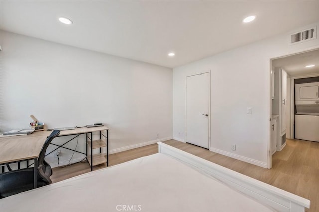 bedroom with stacked washer and clothes dryer and light hardwood / wood-style flooring