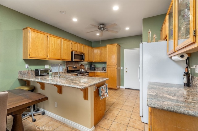 kitchen with appliances with stainless steel finishes, ceiling fan, sink, kitchen peninsula, and light stone counters