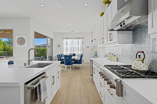 kitchen with wall chimney range hood, white cabinetry, appliances with stainless steel finishes, and sink