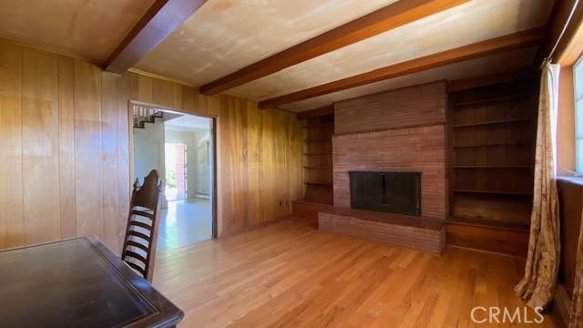 unfurnished living room featuring beam ceiling, a brick fireplace, wooden walls, and light hardwood / wood-style floors