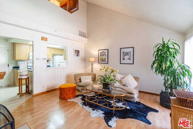 living room featuring high vaulted ceiling, a textured ceiling, and light hardwood / wood-style flooring