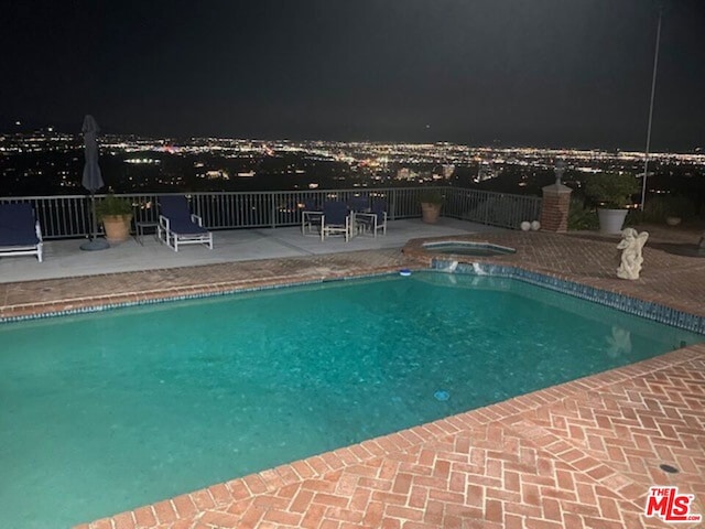 pool at twilight featuring a patio area and an in ground hot tub