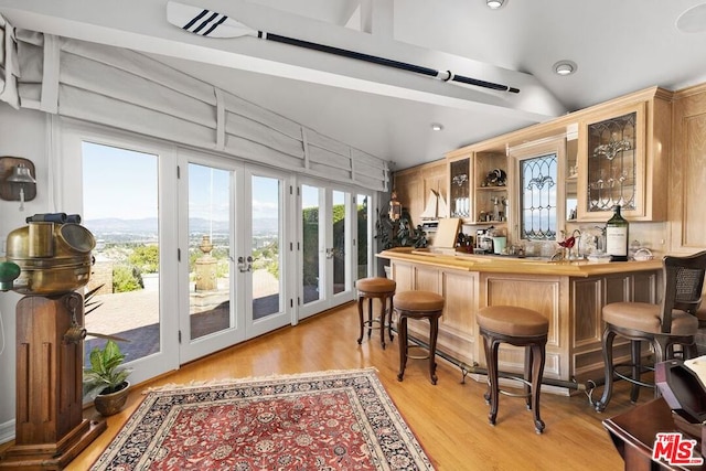 bar featuring light hardwood / wood-style flooring, french doors, and vaulted ceiling