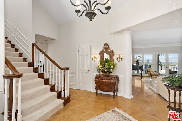 foyer entrance featuring crown molding, a high ceiling, an inviting chandelier, light parquet floors, and ornate columns